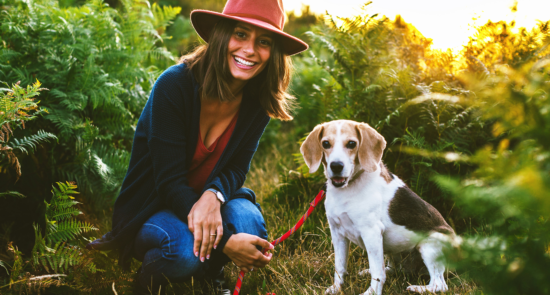 Woman wearing a pink fedora smiling walking a dog